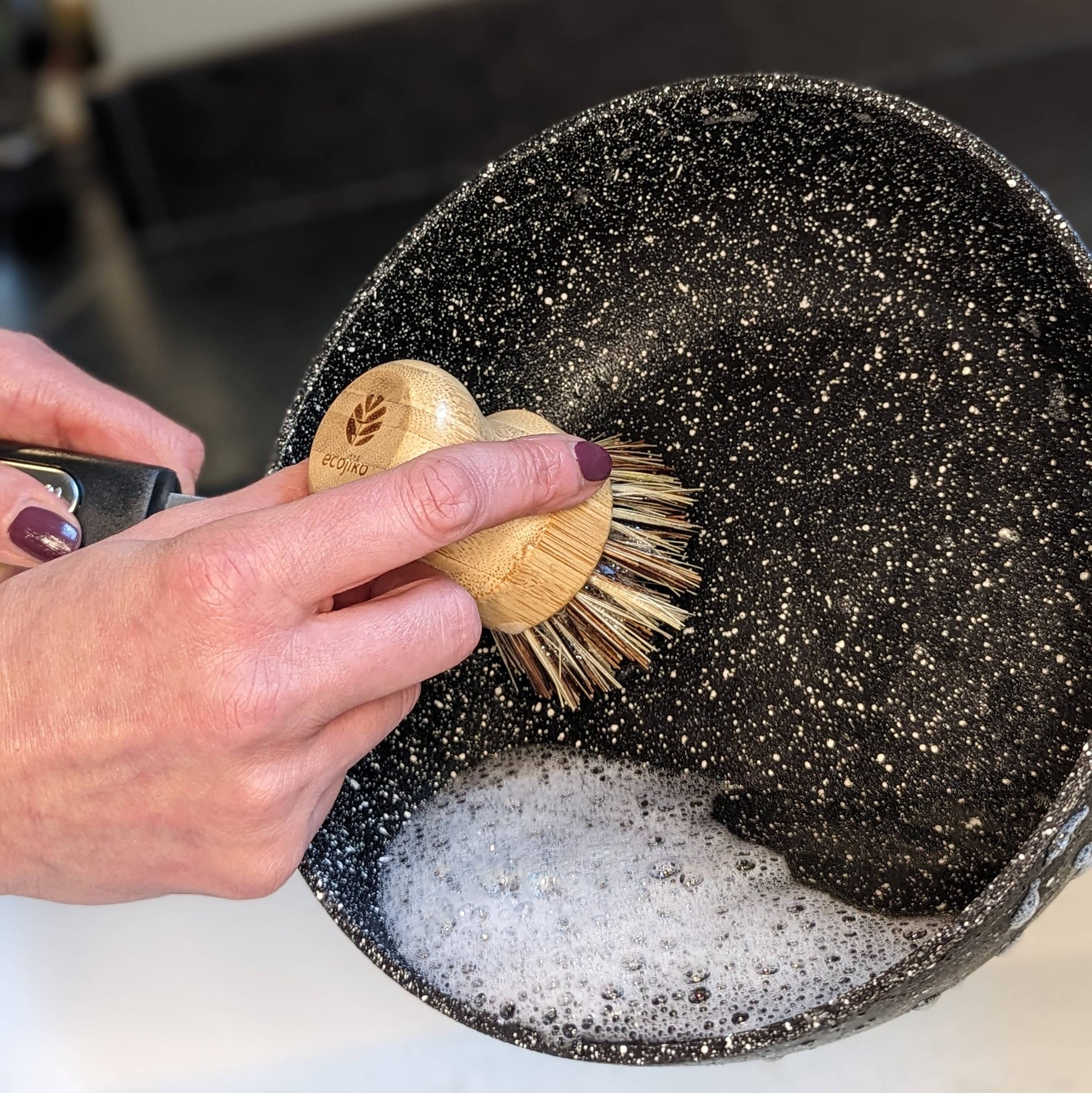 Hand scrubbing a pan with a wooden brush from the Zero Waste Kitchen Cleaning Kit by Churchill and Green