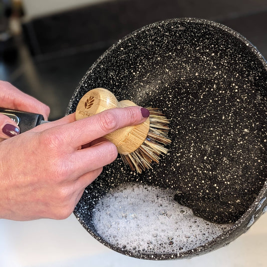 Hand scrubbing a pan with a wooden brush from the Zero Waste Kitchen Cleaning Kit by Churchill and Green