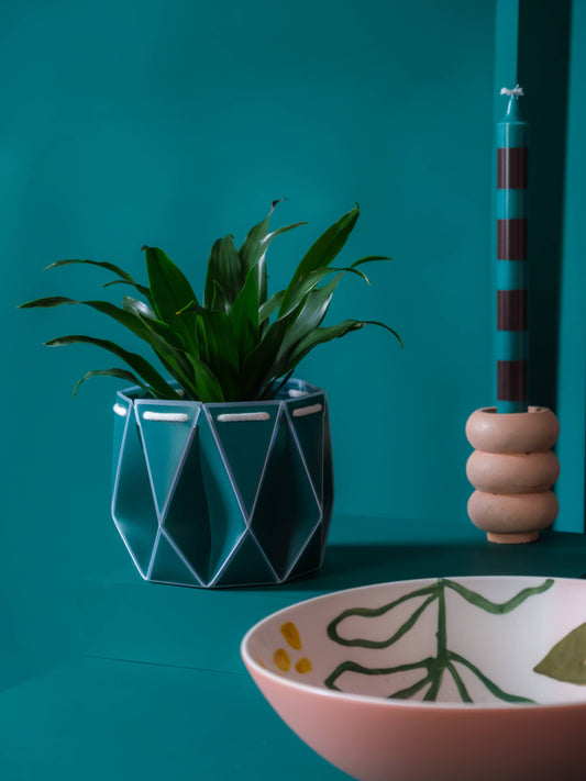 Churchill & Green teal self-watering plant pot with geometric design holding green plant on teal surface